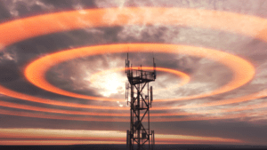 A network tower sends out orange radial signals at sunset