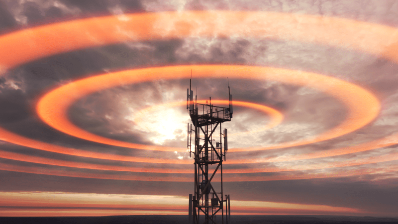 A network tower sends out orange radial signals at sunset
